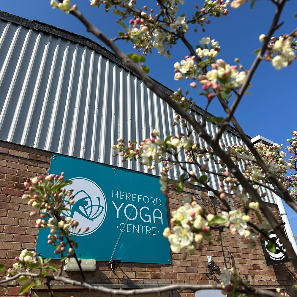 spring photo of herefofrd yoga centre Exterior of Hereford Yoga Centre building with spring blossom in foreground and large HYC sign on front of Foley Industrial Estate building. Blue sky.