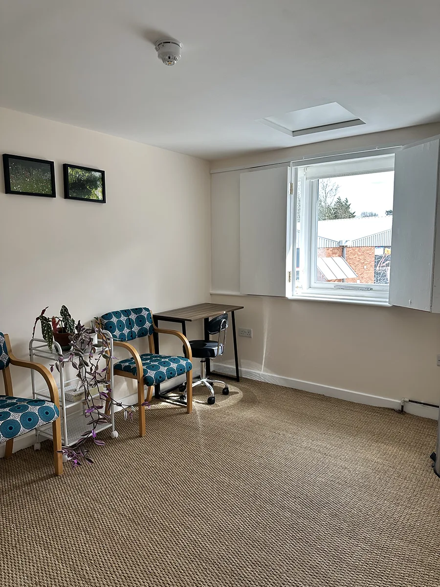 Therapy room consultation area with comfortable seating, desk and natural daylight at Hereford Yoga Centre.